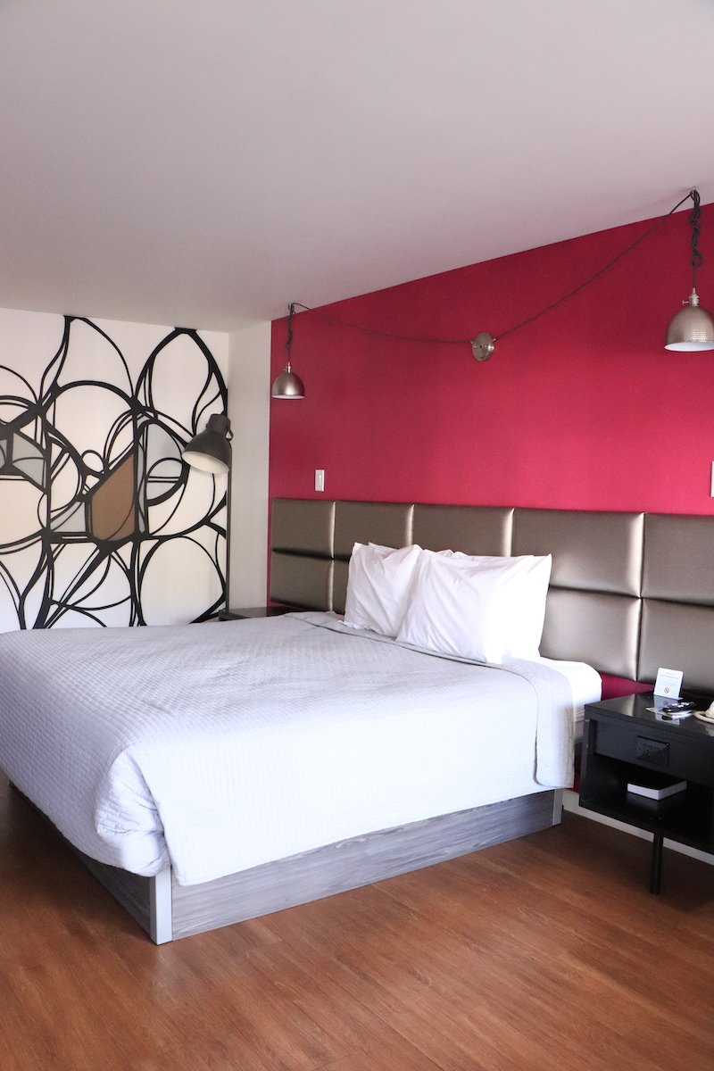1 King Bed — king bed with upholstered headboard, pendant lights, and red accent wall
